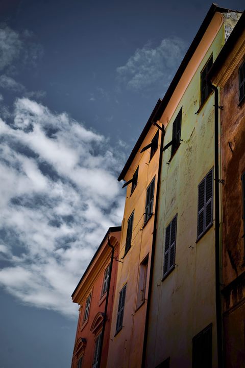 Farbige Hausfassaden von unten gesehen, daneben ein dunkelblauer Himmel mit Wolken