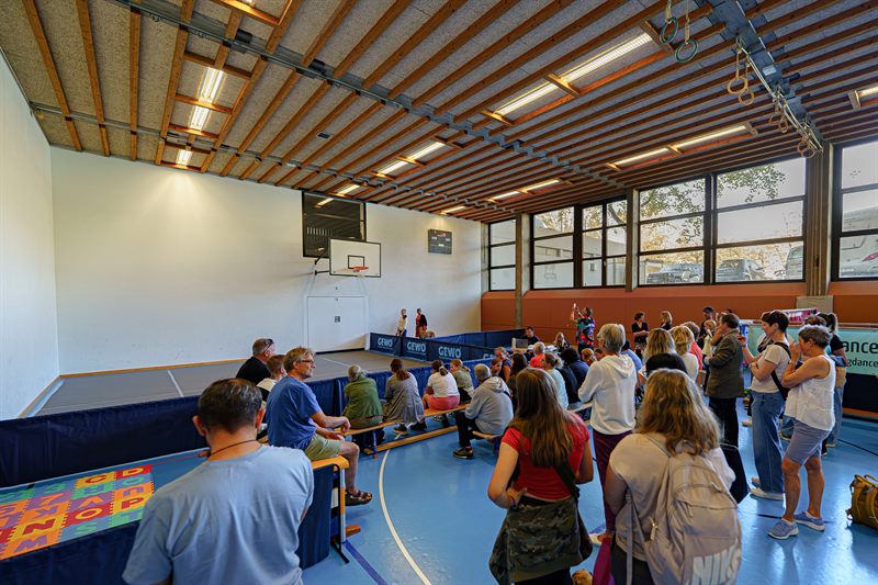Publikum mit Hunden verfolgt eine Vorführung in einer Sporthalle
