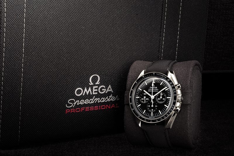 Omega Speedmaster auf einem Uhrenkissen vor der dunklen Schachtel mit Omega-Schriftzug