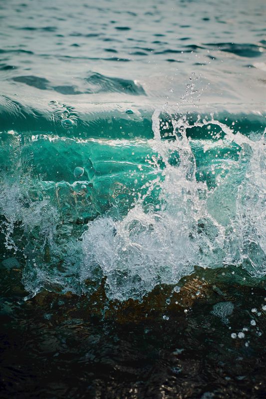 Türkisfarbene Welle bricht am Ufer, das Wasser spritzt auf